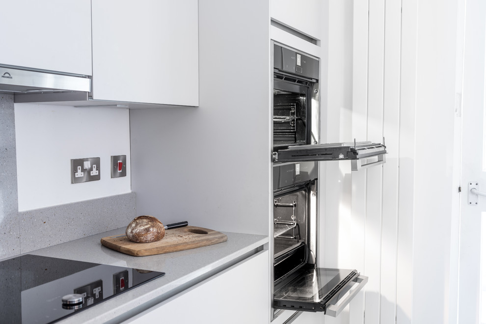 Inspiration for a small contemporary galley separate kitchen in Hampshire with a single-bowl sink, flat-panel cabinets, quartzite benchtops, grey splashback, stone slab splashback, panelled appliances and ceramic floors.