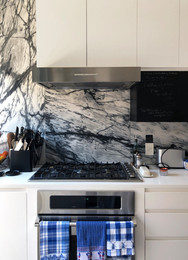 Photo of a mid-sized modern galley kitchen in New York with an undermount sink, flat-panel cabinets, grey splashback, marble splashback, stainless steel appliances, medium hardwood floors, with island, white benchtop and white cabinets.