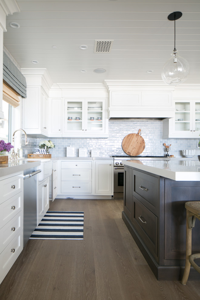 This is an example of a mid-sized beach style u-shaped open plan kitchen in Orange County with a farmhouse sink, shaker cabinets, white cabinets, quartz benchtops, blue splashback, ceramic splashback, stainless steel appliances, light hardwood floors and with island.