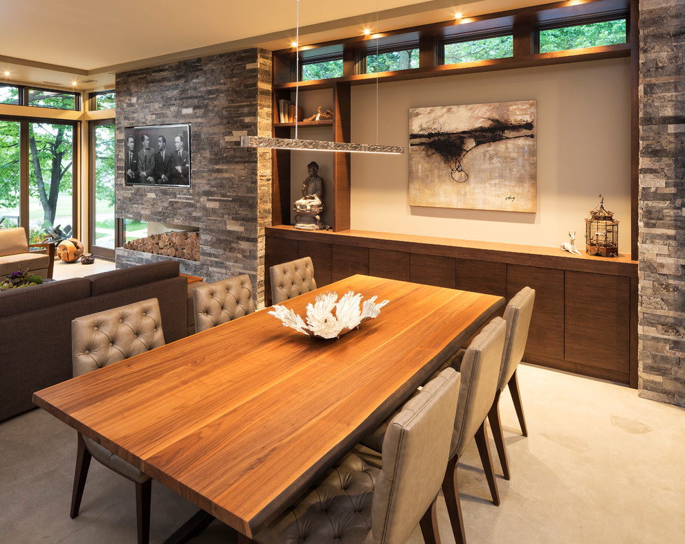 Small modern open plan dining in Minneapolis with beige walls, concrete floors and a stone fireplace surround.