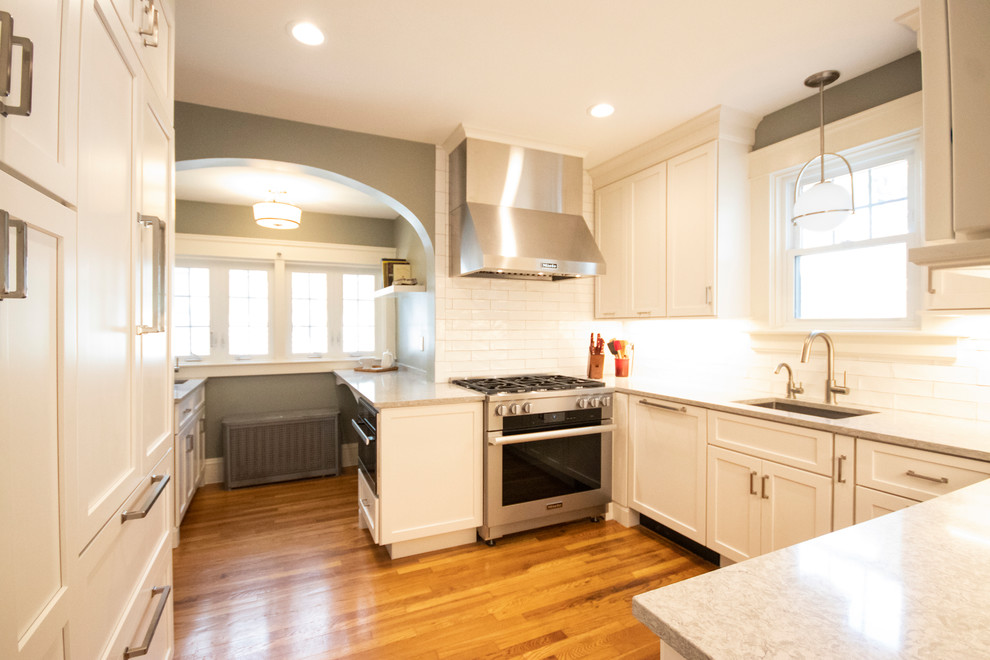 Mid-sized transitional l-shaped medium tone wood floor and brown floor kitchen pantry photo in Providence with an undermount sink, recessed-panel cabinets, white cabinets, quartzite countertops, white backsplash, ceramic backsplash, stainless steel appliances, no island and white countertops