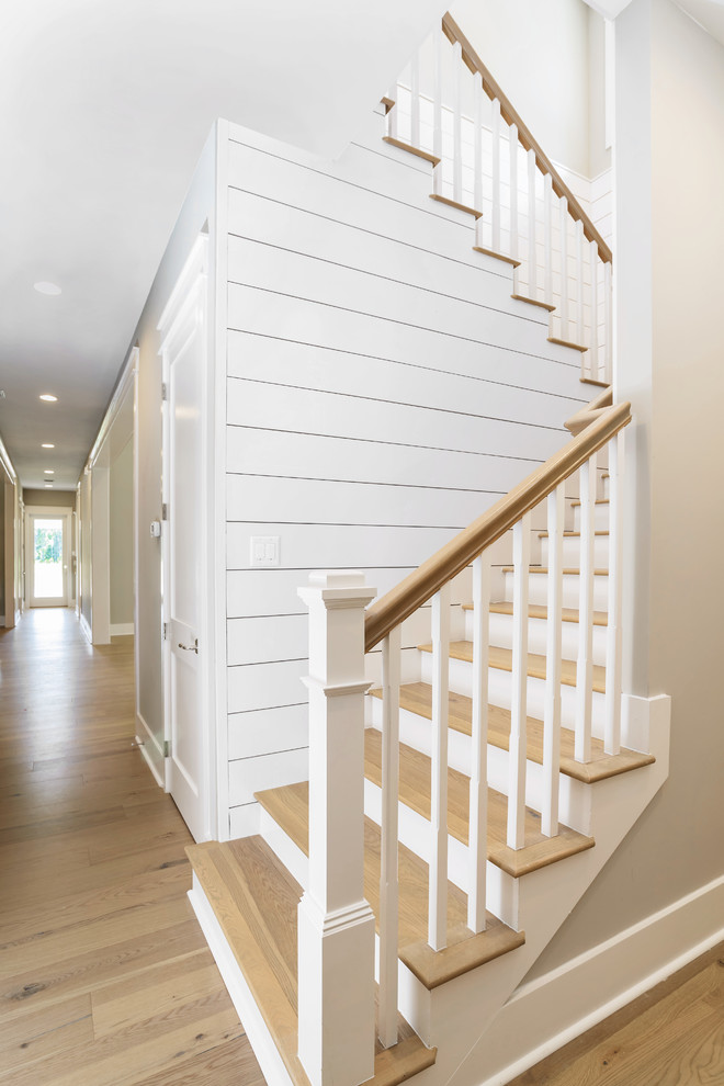 This is an example of a large beach style wood u-shaped staircase in Jacksonville with painted wood risers and wood railing.