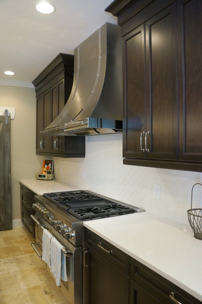 Eat-in kitchen - mid-sized transitional l-shaped travertine floor eat-in kitchen idea in Raleigh with a farmhouse sink, flat-panel cabinets, dark wood cabinets, quartz countertops, white backsplash, ceramic backsplash, stainless steel appliances and an island