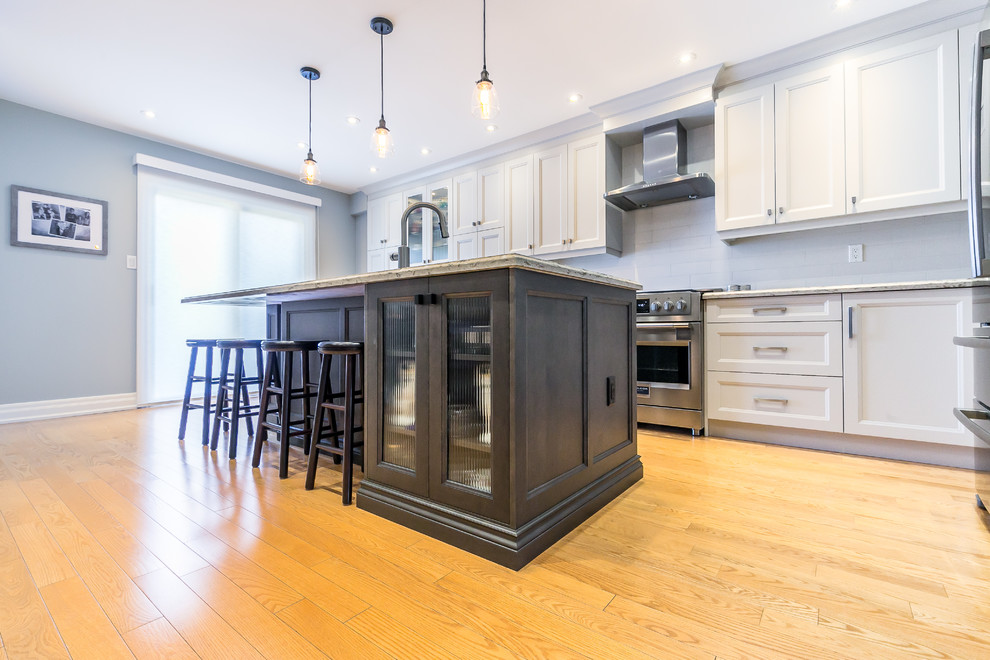 Inspiration for a mid-sized transitional l-shaped brown floor kitchen remodel in Toronto with a double-bowl sink, white cabinets, white backsplash, stainless steel appliances and an island