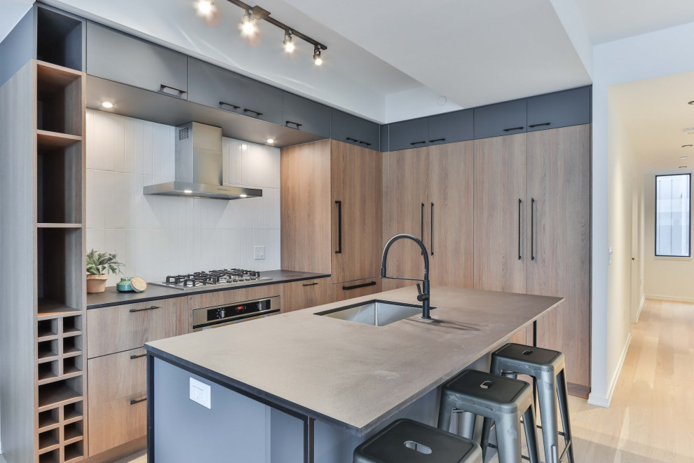 Inspiration for an expansive contemporary l-shaped eat-in kitchen in San Francisco with a drop-in sink, flat-panel cabinets, light wood cabinets, quartzite benchtops, multi-coloured splashback, subway tile splashback, black appliances, laminate floors, with island and brown floor.