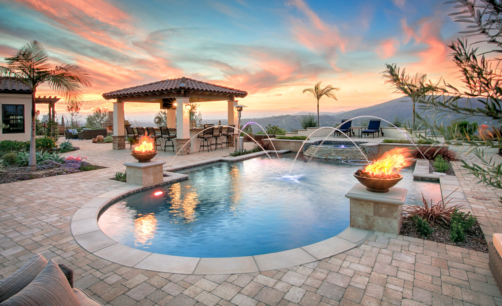 This is an example of a mediterranean backyard custom-shaped lap pool in San Diego with a water feature and natural stone pavers.