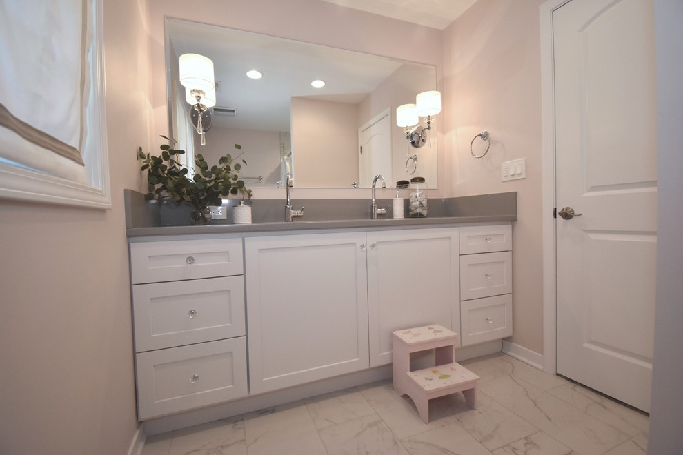 Photo of a mid-sized traditional kids bathroom in Chicago with shaker cabinets, white cabinets, an alcove tub, a shower/bathtub combo, a two-piece toilet, white tile, porcelain tile, pink walls, porcelain floors, a trough sink, engineered quartz benchtops, white floor and a shower curtain.