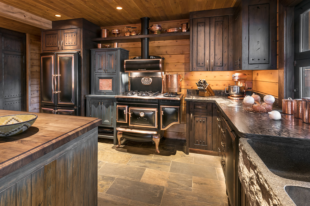 Photo of a large country l-shaped open plan kitchen in Phoenix with a farmhouse sink, raised-panel cabinets, limestone benchtops, timber splashback, black appliances, slate floors, with island, dark wood cabinets and grey floor.