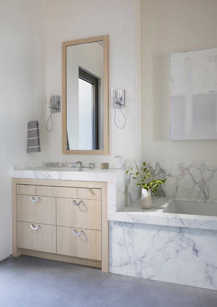 Diseño de cuarto de baño principal, único y a medida minimalista con armarios con paneles lisos, puertas de armario de madera clara, bañera encastrada sin remate, paredes blancas, suelo de cemento y suelo gris