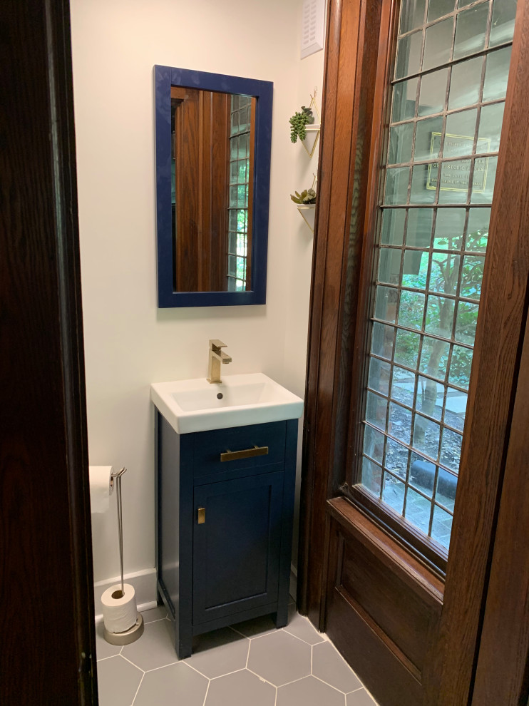 Inspiration for a small arts and crafts powder room in New York with recessed-panel cabinets, blue cabinets, a one-piece toilet, white walls, cement tiles, a vessel sink, grey floor, white benchtops and a freestanding vanity.