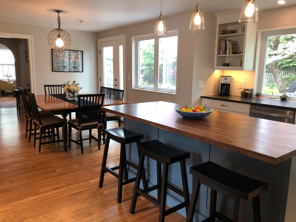 Inspiration for a mid-sized transitional l-shaped medium tone wood floor and brown floor open concept kitchen remodel in Boston with a single-bowl sink, shaker cabinets, white cabinets, granite countertops, white backsplash, window backsplash, stainless steel appliances, an island and black countertops