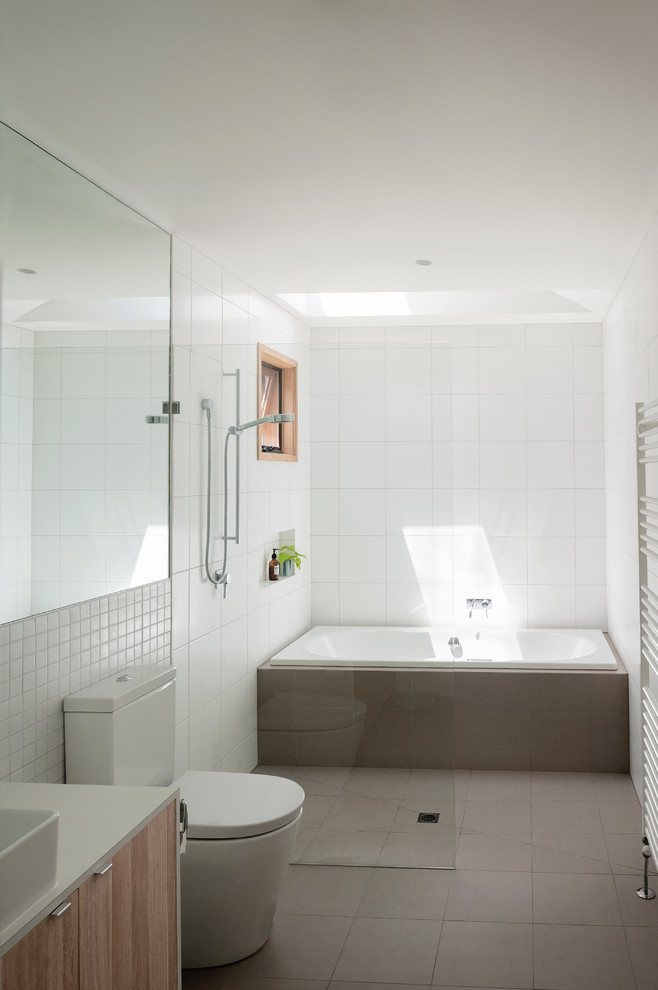 Inspiration for a mid-sized contemporary bathroom in Melbourne with glass-front cabinets, light wood cabinets, an alcove tub, an open shower, a two-piece toilet, white tile, ceramic tile, white walls, ceramic floors, a vessel sink and laminate benchtops.