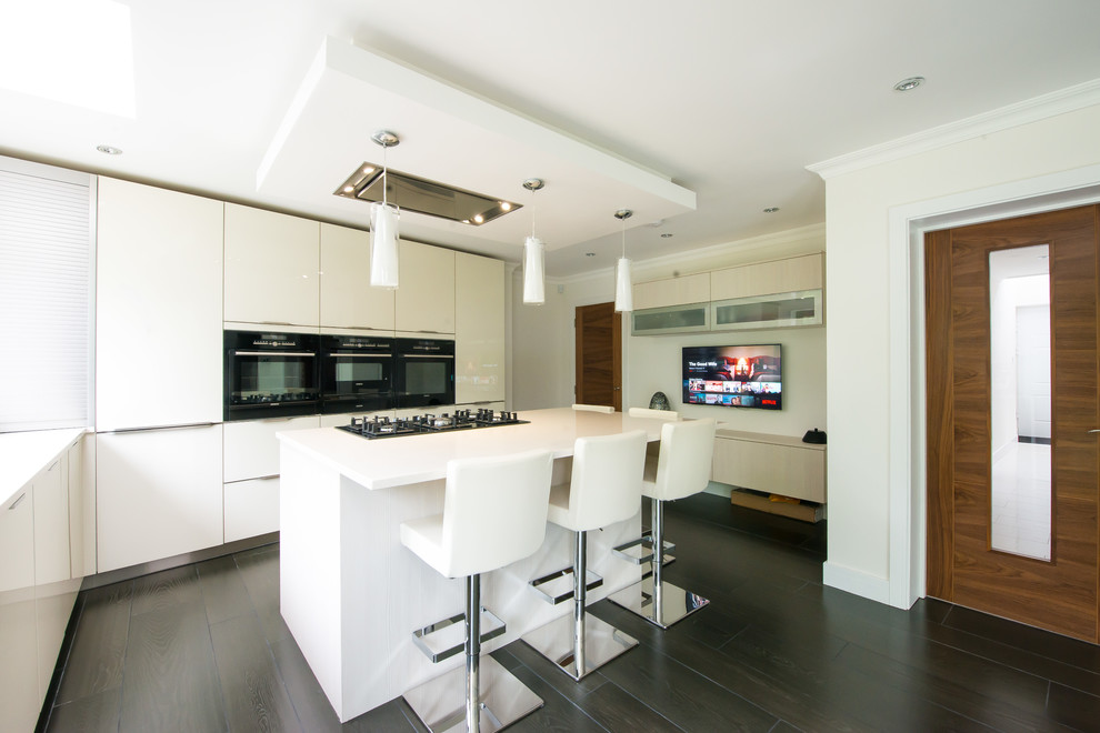 This is an example of a contemporary l-shaped open plan kitchen in London with a drop-in sink, glass-front cabinets, white cabinets, quartzite benchtops, black appliances, porcelain floors and with island.