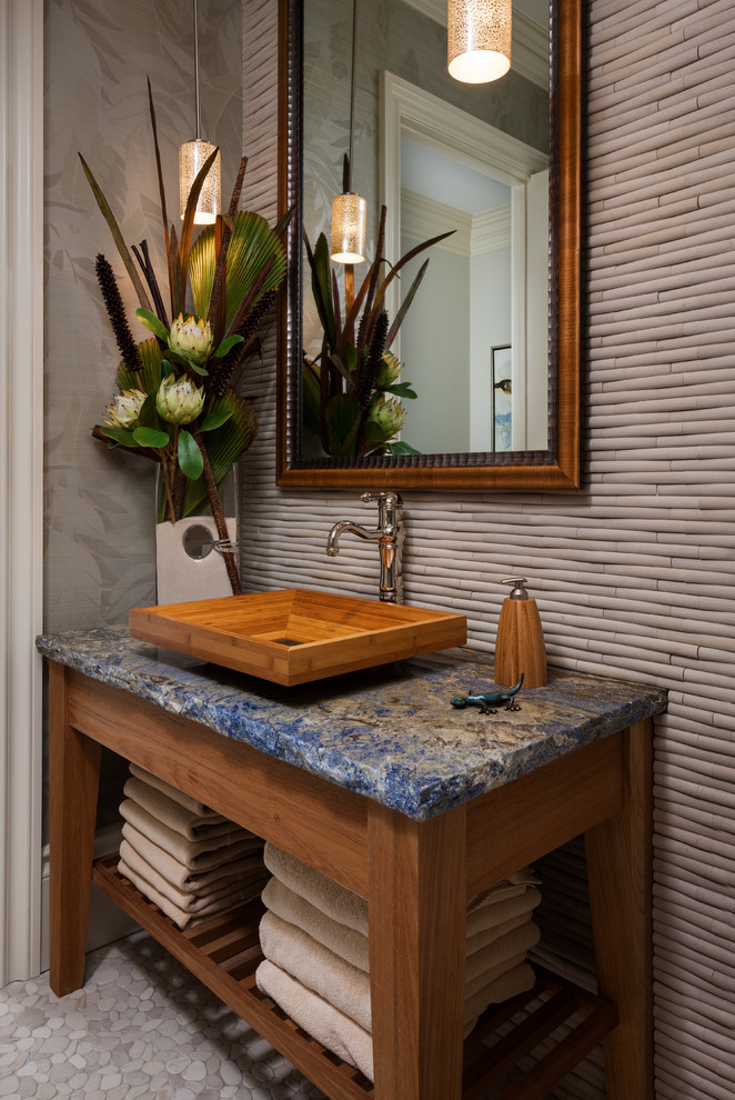 Tropical bathroom in Miami with a vessel sink, medium wood cabinets, beige tile, grey walls, pebble tile floors, open cabinets and blue benchtops.