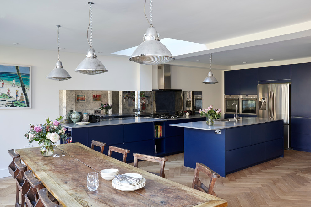 Design ideas for a mid-sized eclectic open plan kitchen in London with an undermount sink, flat-panel cabinets, blue cabinets, quartzite benchtops, metallic splashback, glass sheet splashback, stainless steel appliances and medium hardwood floors.
