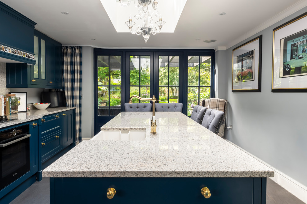 This is an example of a classic kitchen/diner in London with blue cabinets, granite worktops, white splashback, granite splashback, an island, grey floors and white worktops.