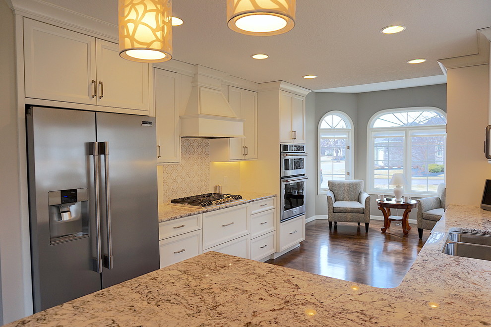 Example of a huge transitional l-shaped medium tone wood floor eat-in kitchen design with an undermount sink, flat-panel cabinets, white cabinets, granite countertops, white backsplash, stone tile backsplash and stainless steel appliances