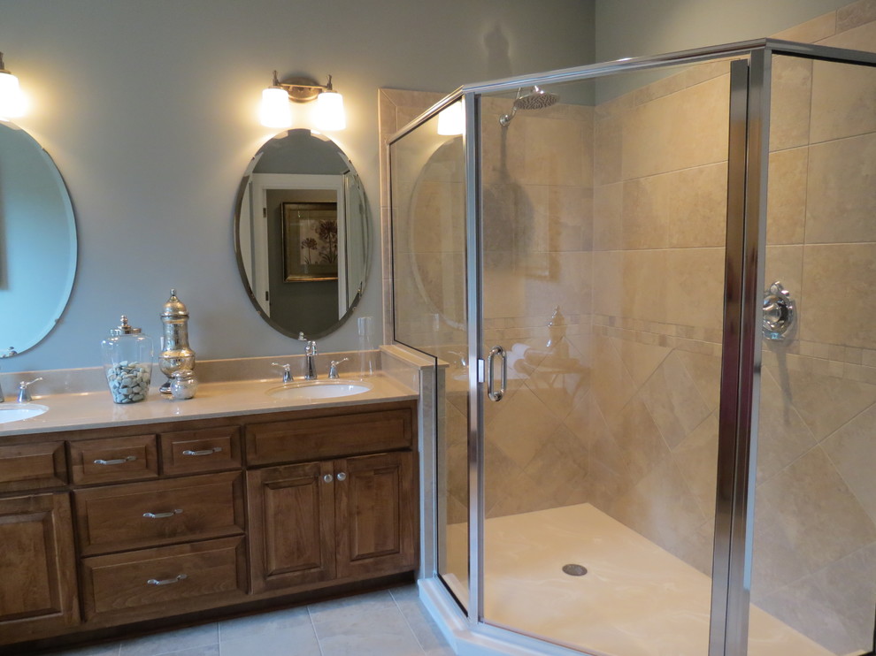Photo of a master bathroom with raised-panel cabinets, light wood cabinets, a drop-in tub, a corner shower, grey walls, an undermount sink, grey floor, a hinged shower door, beige benchtops, a double vanity and a built-in vanity.