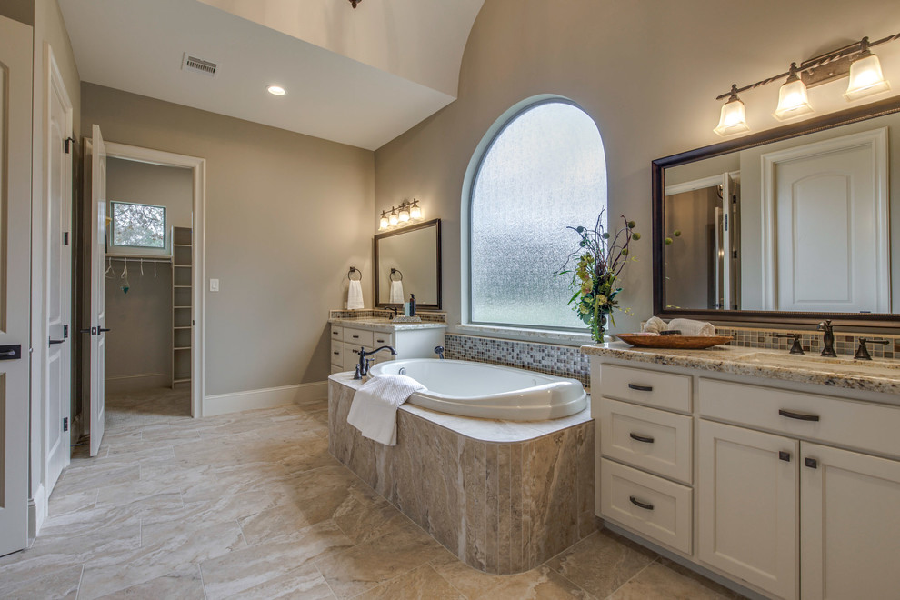 Large mediterranean master bathroom in Houston with a drop-in tub, an undermount sink, granite benchtops, beige floor, furniture-like cabinets, white cabinets, beige tile, mosaic tile, beige walls and ceramic floors.