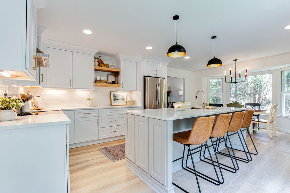 Design ideas for a mid-sized contemporary l-shaped eat-in kitchen in Atlanta with a single-bowl sink, shaker cabinets, white cabinets, quartz benchtops, white splashback, subway tile splashback, stainless steel appliances, laminate floors, with island, beige floor and white benchtop.
