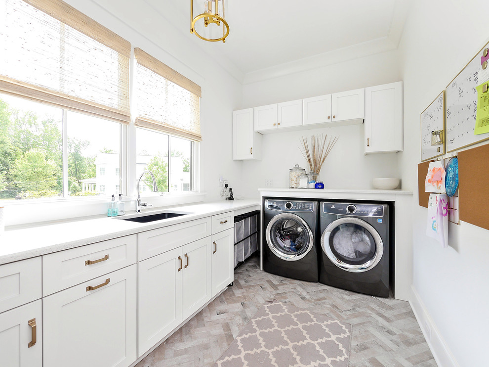 This is an example of a country l-shaped laundry room in Charlotte with an undermount sink, shaker cabinets, white cabinets, a side-by-side washer and dryer, grey floor and white benchtop.