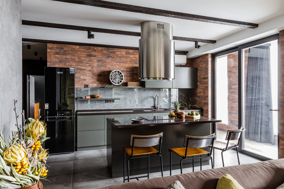 This is an example of a mid-sized industrial single-wall open plan kitchen in Other with flat-panel cabinets, grey cabinets, solid surface benchtops, grey splashback, glass sheet splashback, porcelain floors, with island, grey floor and black benchtop.