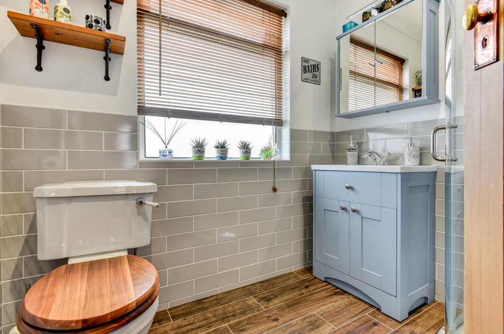 This is an example of a small classic grey and white bathroom in Sussex with shaker cabinets, blue cabinets, a corner shower, a two-piece toilet, beige tiles, ceramic tiles, white walls, a built-in sink, brown floors, a sliding door, feature lighting, a single sink and a freestanding vanity unit.