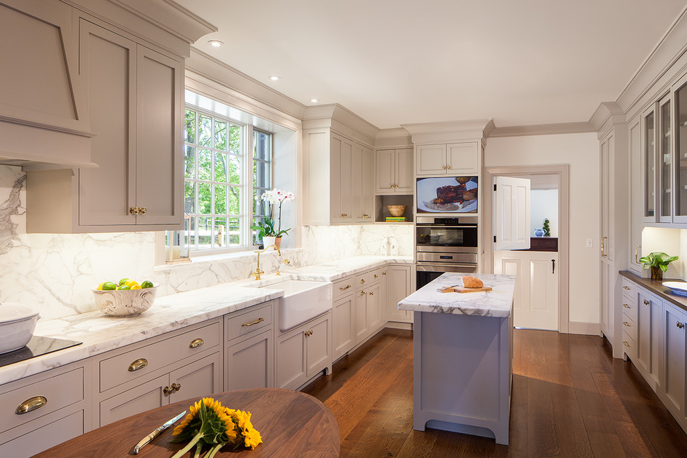 This is an example of a large transitional u-shaped eat-in kitchen in New York with a farmhouse sink, shaker cabinets, white cabinets, marble benchtops, white splashback, marble splashback, stainless steel appliances, medium hardwood floors, with island and brown floor.