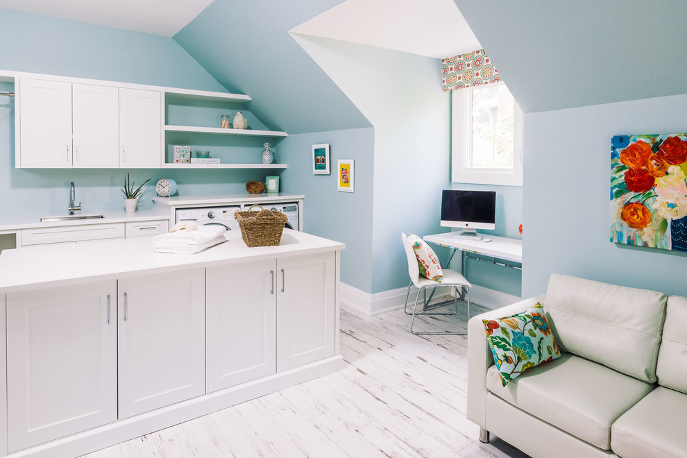 This is an example of a transitional utility room in Other with an undermount sink, shaker cabinets, white cabinets, blue walls, painted wood floors, a side-by-side washer and dryer and white floor.