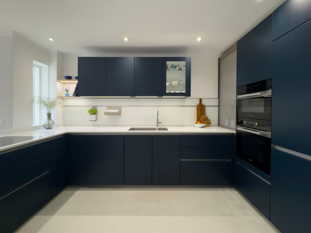 Mid-sized contemporary u-shaped eat-in kitchen in Other with an integrated sink, flat-panel cabinets, blue cabinets, quartzite benchtops, white splashback, glass sheet splashback, black appliances and white benchtop.