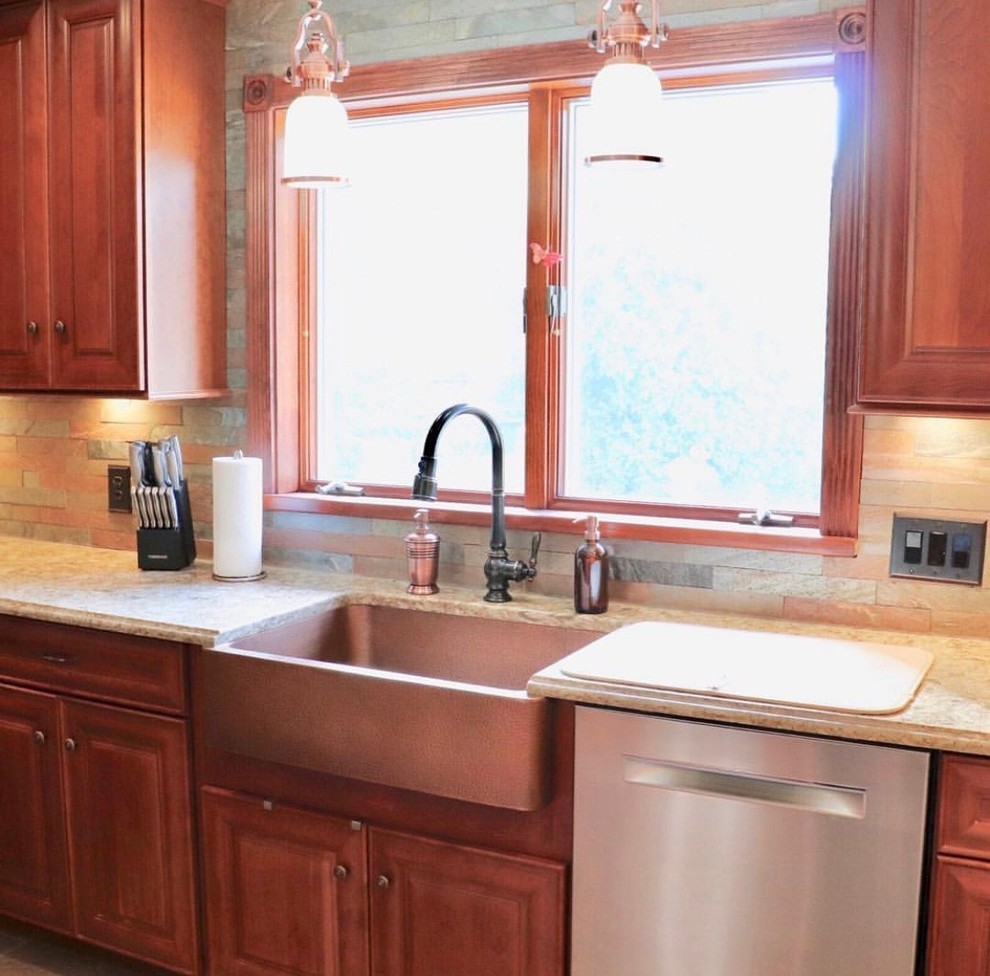 This is an example of a mid-sized traditional u-shaped separate kitchen in New York with a farmhouse sink, raised-panel cabinets, medium wood cabinets, quartz benchtops, brown splashback, slate splashback, stainless steel appliances, vinyl floors, with island, multi-coloured floor and beige benchtop.