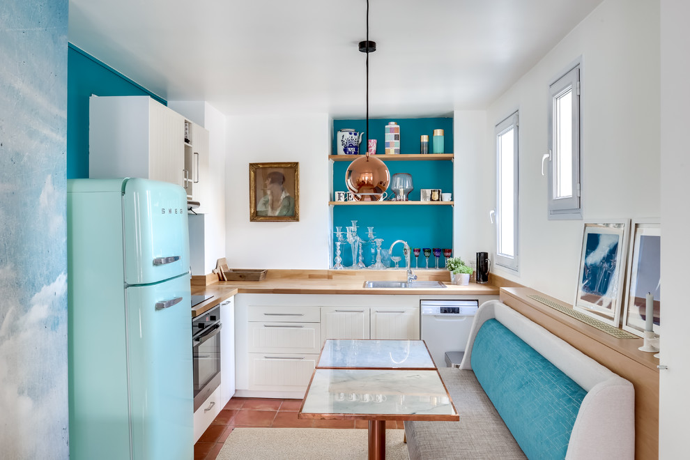 Inspiration for a mid-sized eclectic l-shaped eat-in kitchen in Paris with wood benchtops, coloured appliances, terra-cotta floors, brown floor, a drop-in sink, white cabinets and blue splashback.
