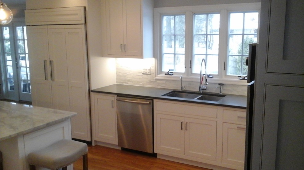 Eat-in kitchen - mid-sized transitional l-shaped light wood floor eat-in kitchen idea in Newark with a double-bowl sink, shaker cabinets, white cabinets, solid surface countertops, multicolored backsplash, stone tile backsplash, stainless steel appliances and an island