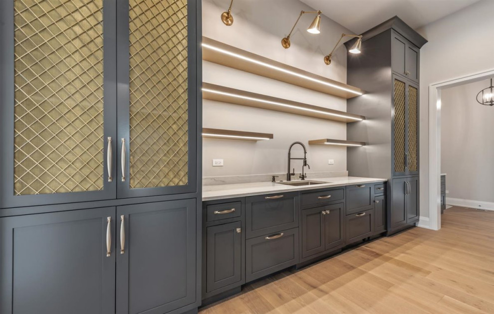 This is an example of a mid-sized transitional galley kitchen pantry in Chicago with an undermount sink, shaker cabinets, grey cabinets, quartz benchtops, white splashback, engineered quartz splashback, panelled appliances, light hardwood floors, no island, brown floor and white benchtop.