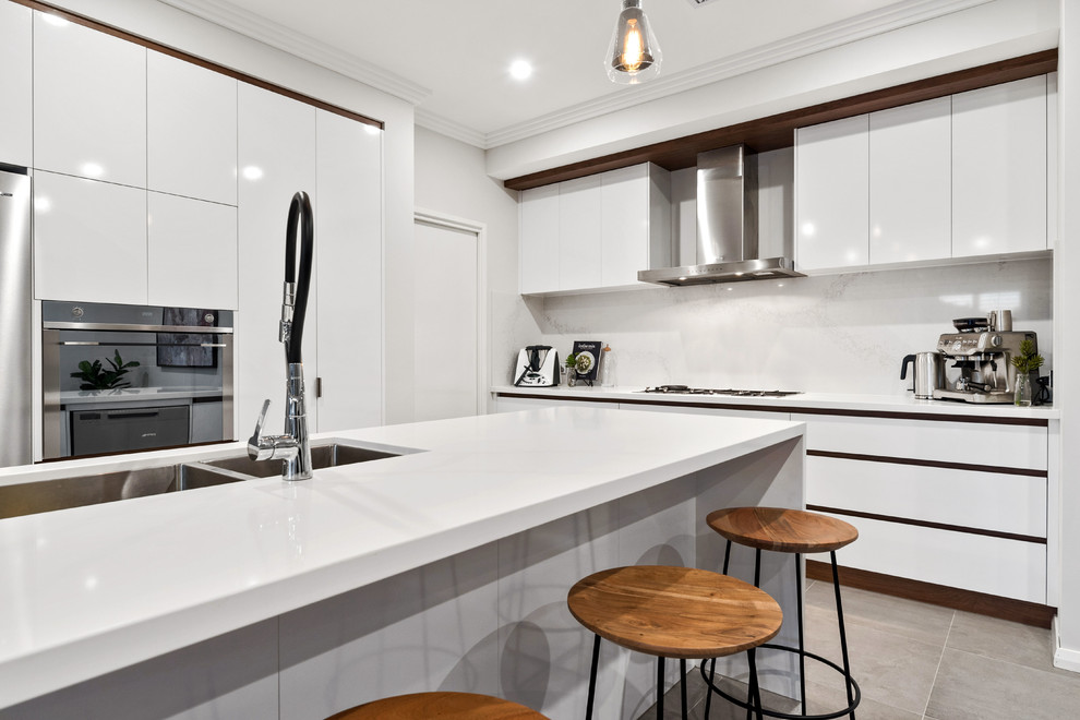 Photo of a contemporary l-shaped kitchen in Perth with an undermount sink, flat-panel cabinets, white cabinets, white splashback, stone slab splashback, stainless steel appliances, with island, grey floor and white benchtop.