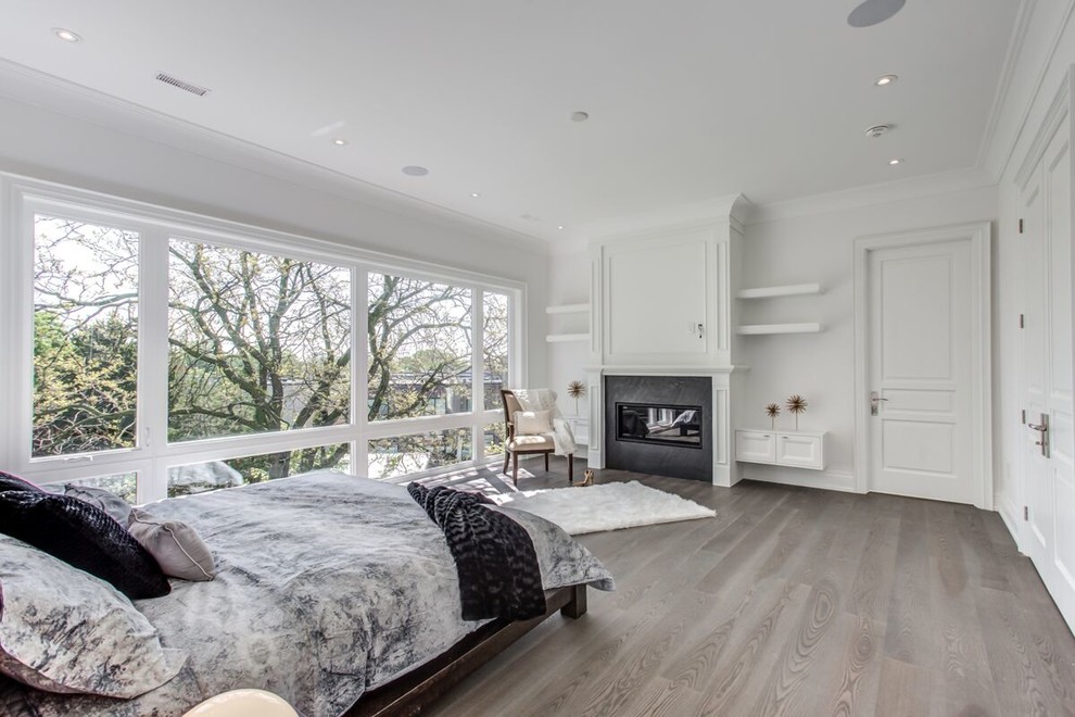 Photo of an expansive modern master bedroom in Toronto with white walls, laminate floors, a standard fireplace, a plaster fireplace surround and grey floor.