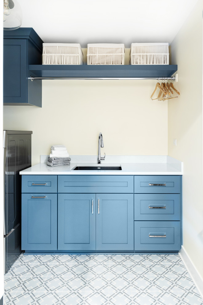 Inspiration for a mid-sized contemporary galley dedicated laundry room in Chicago with an undermount sink, shaker cabinets, blue cabinets, quartz benchtops, white splashback, engineered quartz splashback, yellow walls, ceramic floors, a side-by-side washer and dryer, multi-coloured floor and white benchtop.