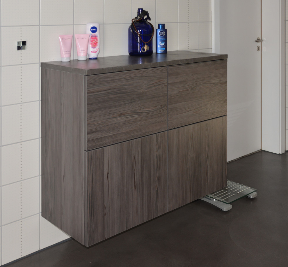 Duschbad With flächenbündigen Schrankfronten, braunen Schränken, Einbaubadewanne, bodengleicher Dusche, Wandtoilette, weißen Fliesen, weißer Wandfarbe, Betonboden, Einbauwaschbecken, Mineralwerkstoff-Waschtisch, grauem Boden, offener Dusche and weißer Waschtischplatte in Nuremberg