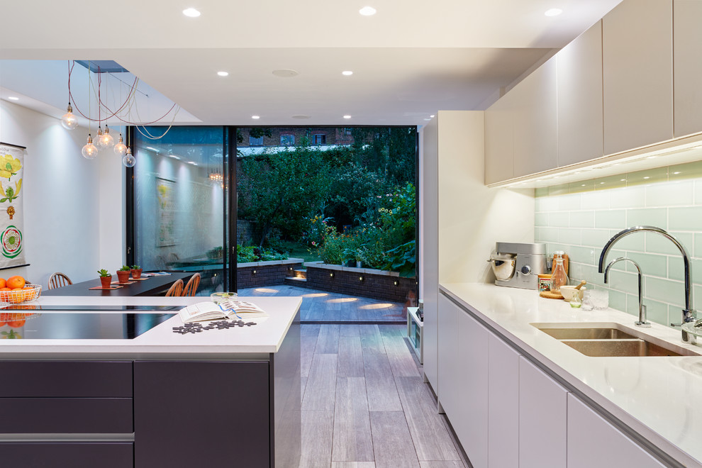Large contemporary single-wall eat-in kitchen in London with a drop-in sink, flat-panel cabinets, white cabinets, solid surface benchtops, blue splashback, glass tile splashback, panelled appliances, porcelain floors and with island.