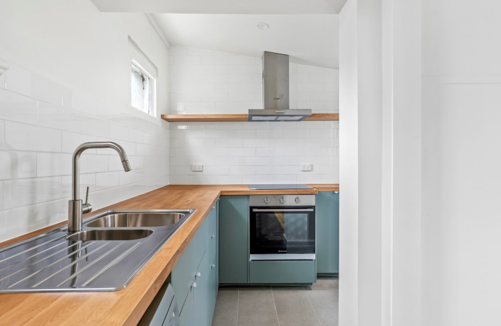 L-shaped kitchen in Other with a double-bowl sink, flat-panel cabinets, green cabinets, laminate countertops, white splashback, metro tiled splashback, stainless steel appliances, grey floors and brown worktops.