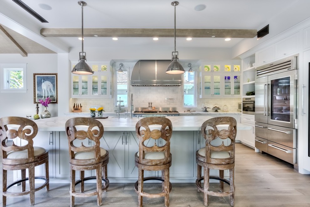 Photo of a large country l-shaped open plan kitchen in Orange County with a farmhouse sink, recessed-panel cabinets, white cabinets, marble benchtops, white splashback, subway tile splashback, stainless steel appliances, light hardwood floors and with island.