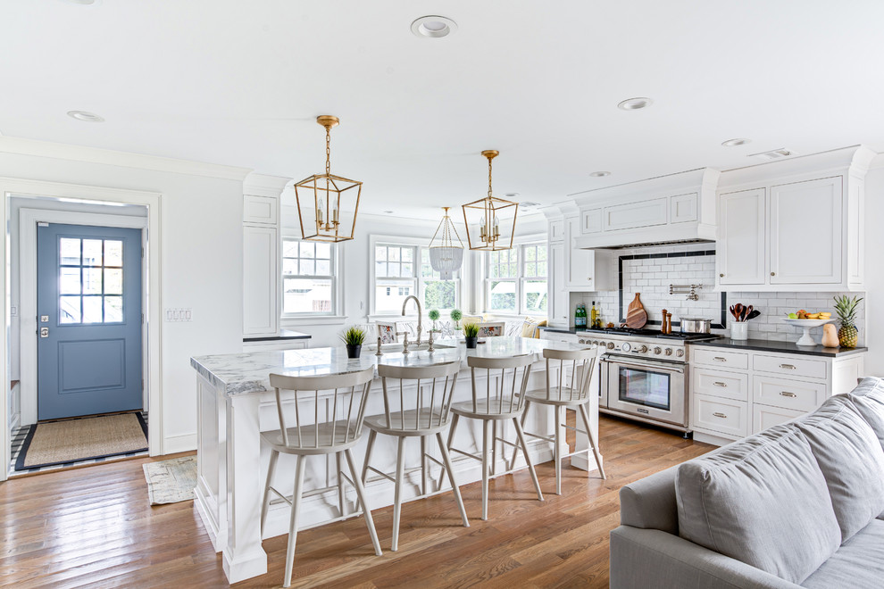 Example of a transitional galley medium tone wood floor and brown floor open concept kitchen design in New York with an undermount sink, shaker cabinets, white cabinets, white backsplash, subway tile backsplash, stainless steel appliances and an island