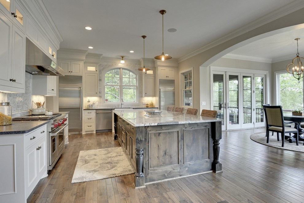 Inspiration for a large transitional l-shaped eat-in kitchen in Minneapolis with a farmhouse sink, beaded inset cabinets, white cabinets, granite benchtops, white splashback, subway tile splashback, stainless steel appliances, medium hardwood floors and with island.