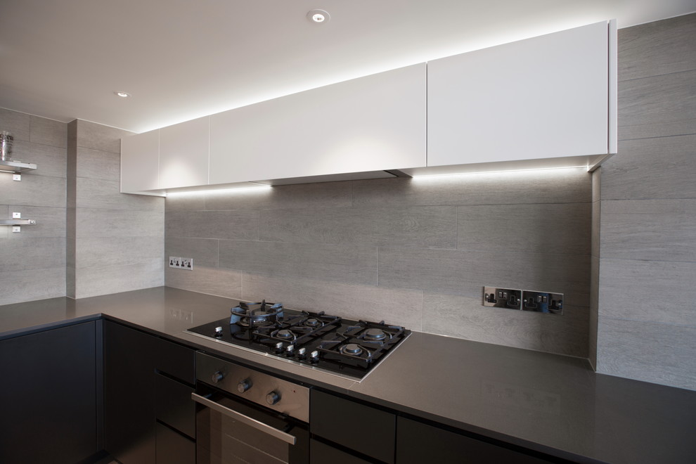 This is an example of a small industrial u-shaped open plan kitchen in London with a drop-in sink, flat-panel cabinets, grey cabinets, quartz benchtops, grey splashback, ceramic splashback, panelled appliances, light hardwood floors and a peninsula.