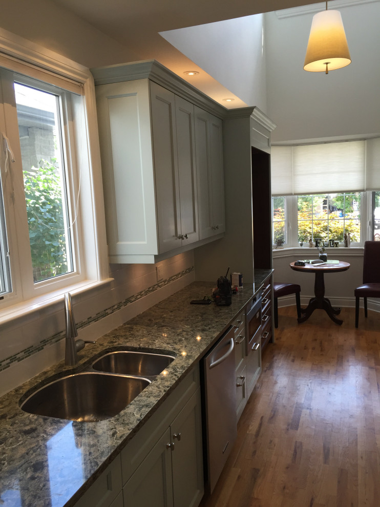 Mid-sized transitional single-wall medium tone wood floor and brown floor enclosed kitchen photo in Ottawa with a double-bowl sink, recessed-panel cabinets, gray cabinets, granite countertops, porcelain backsplash, stainless steel appliances and gray countertops