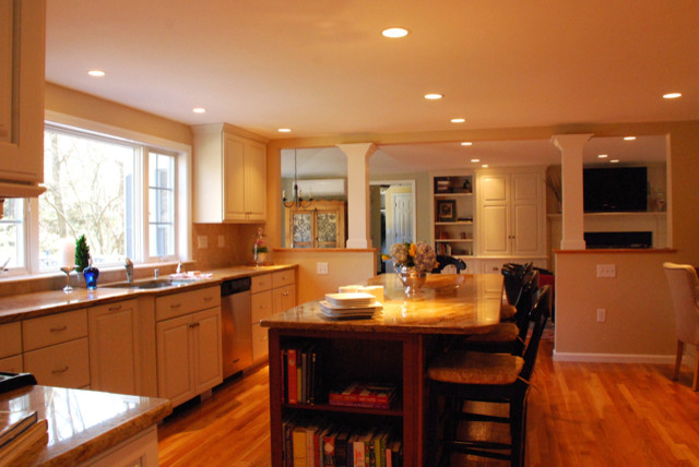 Photo of a traditional l-shaped eat-in kitchen in Boston with an undermount sink, raised-panel cabinets, white cabinets, granite benchtops, beige splashback, stone tile splashback, stainless steel appliances, medium hardwood floors and with island.