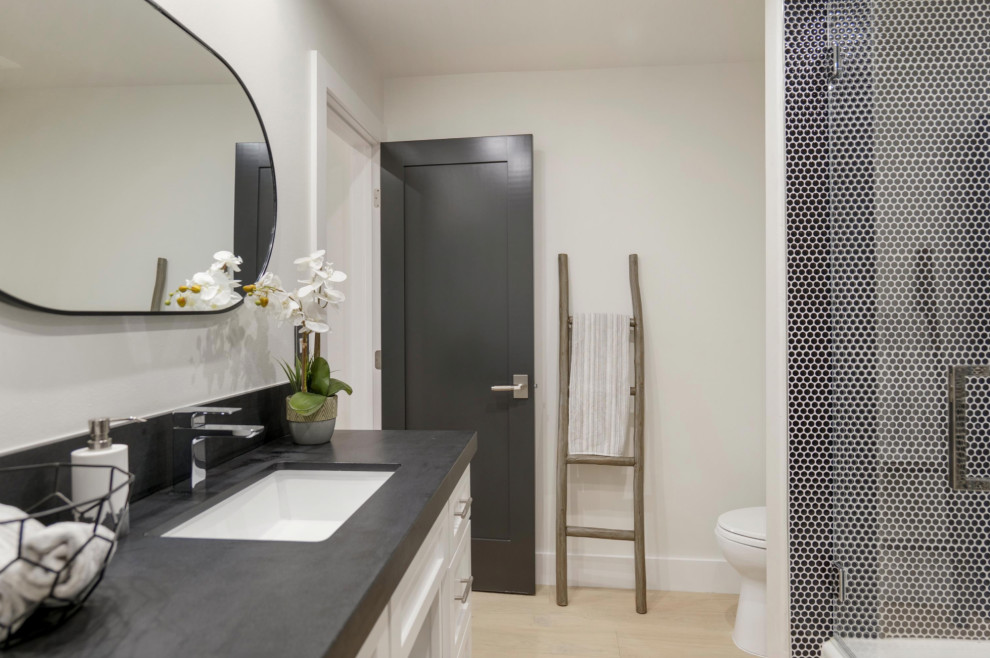 This is an example of a mid-sized midcentury 3/4 bathroom in Orange County with shaker cabinets, white cabinets, an alcove tub, a shower/bathtub combo, a one-piece toilet, white tile, ceramic tile, white walls, light hardwood floors, an undermount sink, engineered quartz benchtops, a hinged shower door, black benchtops, a single vanity and a built-in vanity.