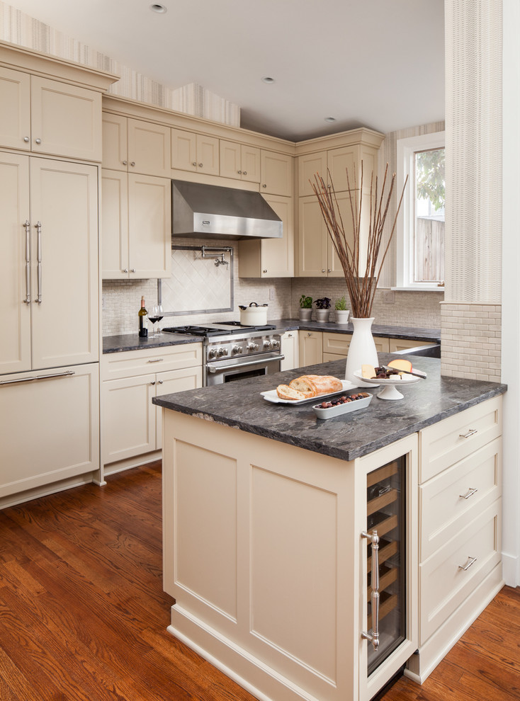Mid-sized transitional u-shaped open plan kitchen in DC Metro with a farmhouse sink, recessed-panel cabinets, beige cabinets, granite benchtops, beige splashback, ceramic splashback, stainless steel appliances, medium hardwood floors, a peninsula and brown floor.