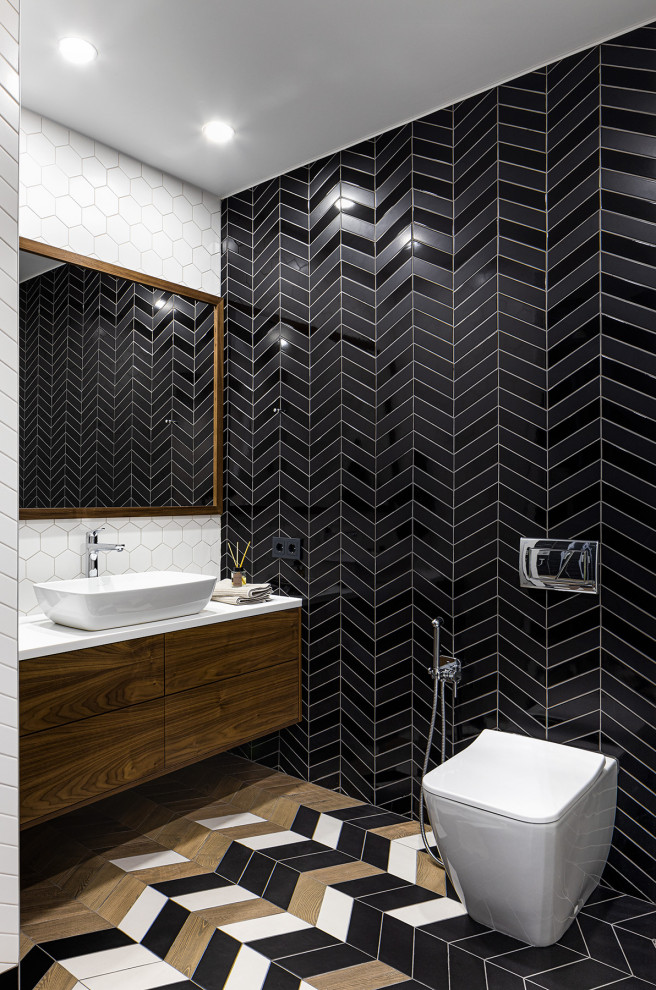 Inspiration for a mid-sized contemporary bathroom in Moscow with flat-panel cabinets, medium wood cabinets, an alcove shower, a wall-mount toilet, black and white tile, ceramic tile, black walls, ceramic floors, a drop-in sink, solid surface benchtops, multi-coloured floor, a sliding shower screen and white benchtops.
