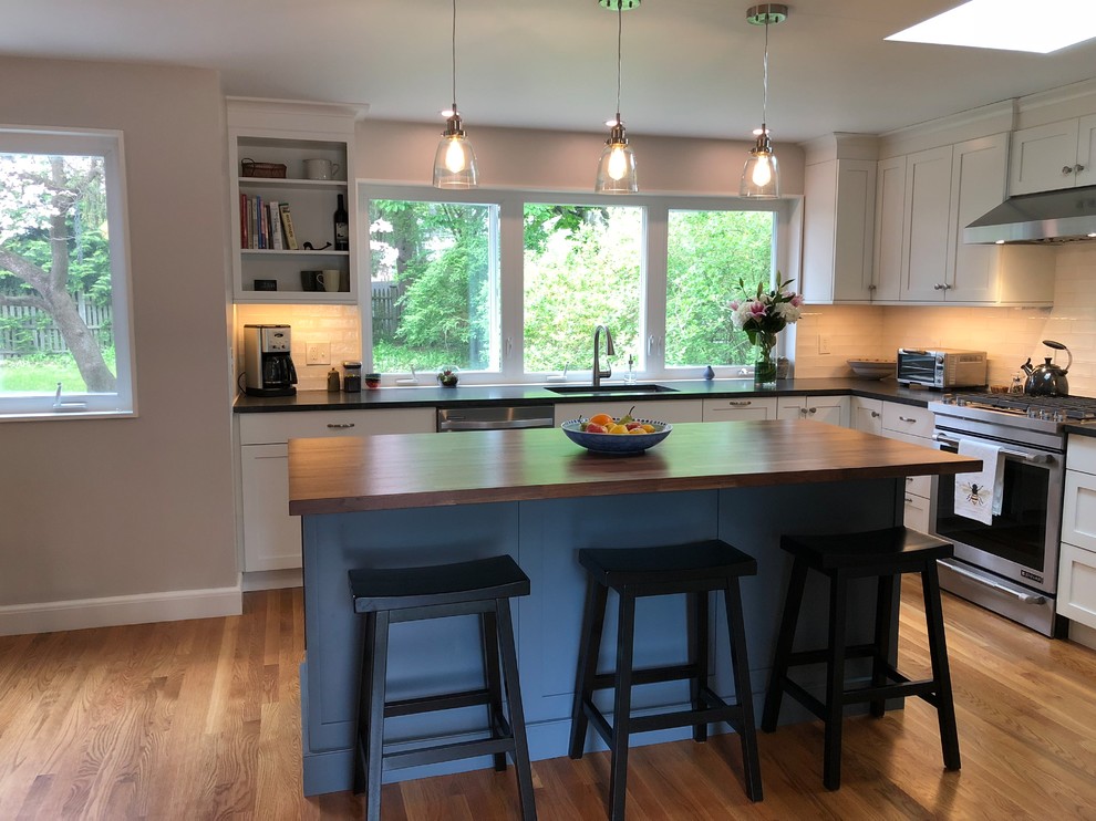 Open concept kitchen - mid-sized transitional l-shaped medium tone wood floor and brown floor open concept kitchen idea in Boston with a single-bowl sink, shaker cabinets, white cabinets, granite countertops, white backsplash, window backsplash, stainless steel appliances, an island and black countertops